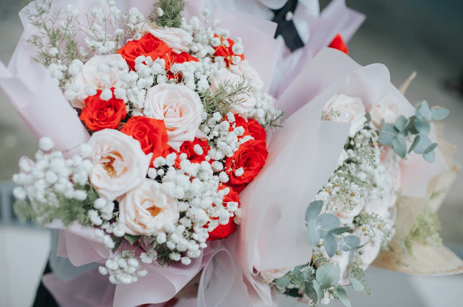 A close-up image of a floral bouquet featuring a combination of white and red roses, complemented by delicate sprigs of baby's breath and pale green eucalyptus leaves. The flowers are arranged in a lu